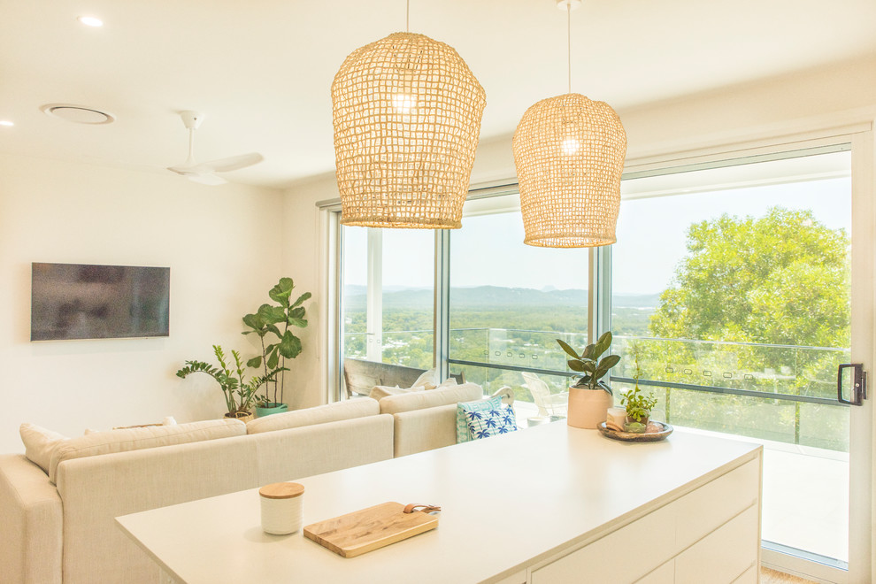 This is an example of a large contemporary l-shaped open plan kitchen in Sunshine Coast with flat-panel cabinets, white cabinets, quartz benchtops, white splashback, ceramic splashback, light hardwood floors, with island and white benchtop.