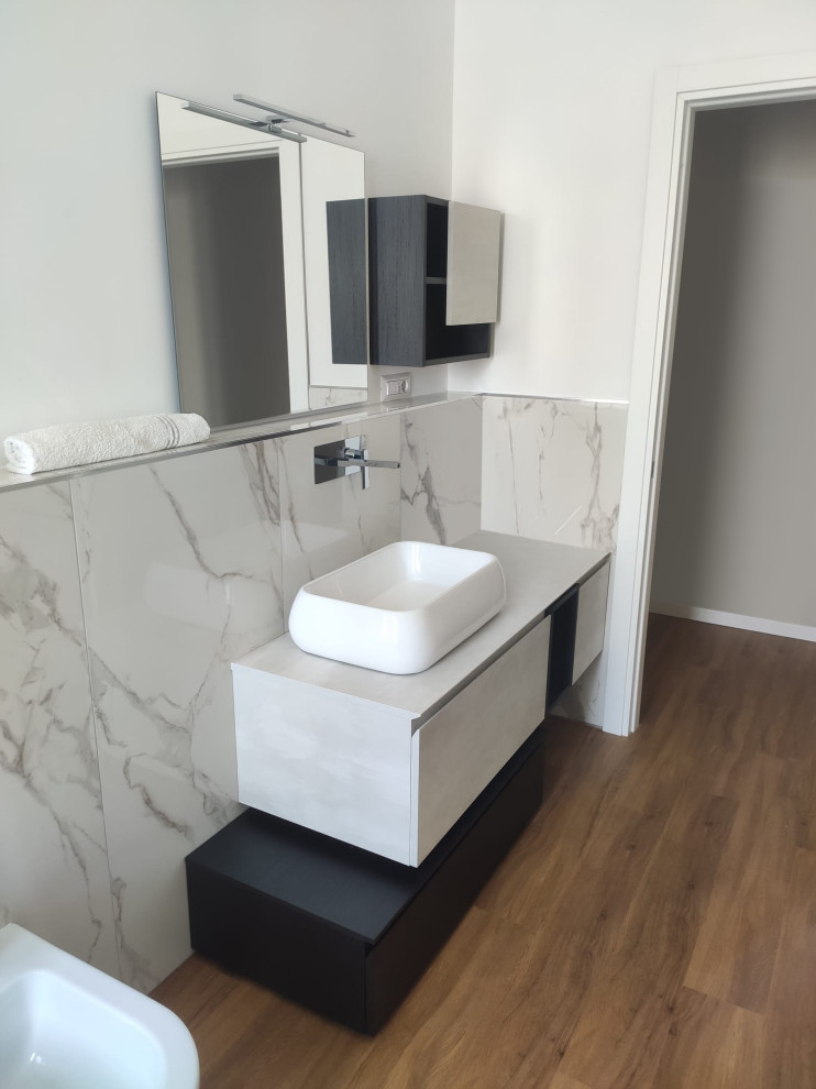 This is an example of a mid-sized contemporary 3/4 bathroom in Cagliari with grey cabinets, black and white tile, porcelain tile, grey walls, laminate floors, solid surface benchtops, brown floor, grey benchtops, a single vanity, a floating vanity, a two-piece toilet, a vessel sink and a hinged shower door.