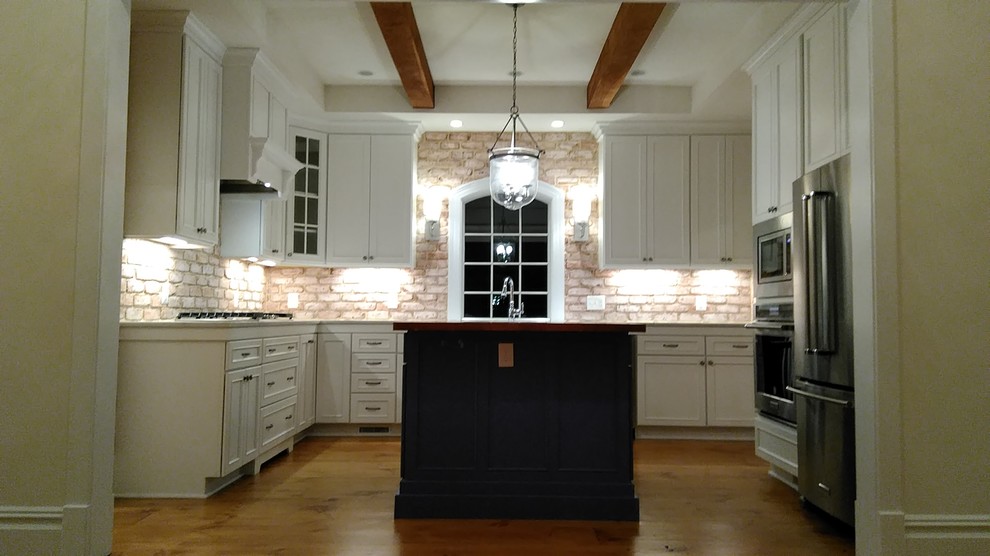 Inspiration for a mid-sized arts and crafts u-shaped open plan kitchen in DC Metro with an undermount sink, recessed-panel cabinets, white cabinets, marble benchtops, beige splashback, brick splashback, stainless steel appliances, medium hardwood floors, with island and brown floor.