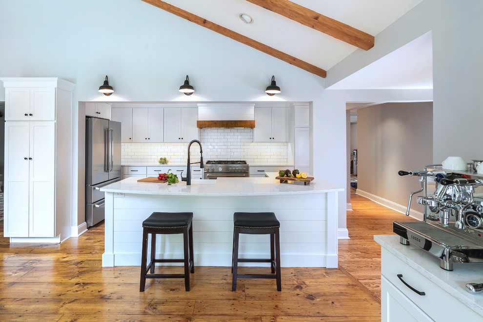 Mid-sized country galley open plan kitchen in Philadelphia with a farmhouse sink, white cabinets, white splashback, subway tile splashback, stainless steel appliances, medium hardwood floors, with island, brown floor, white benchtop, quartz benchtops and recessed-panel cabinets.