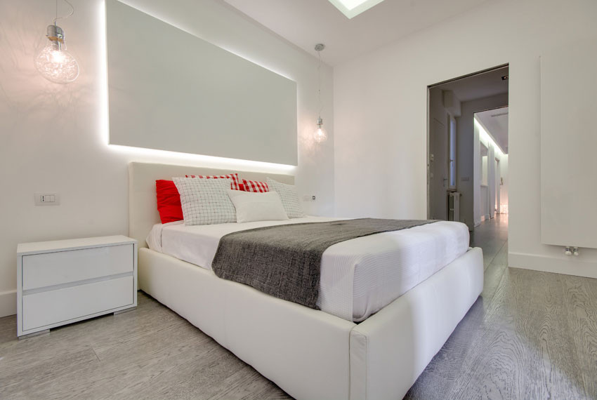 This is an example of an expansive modern master bedroom in Rome with white walls, light hardwood floors, a hanging fireplace, a plaster fireplace surround, beige floor and recessed.