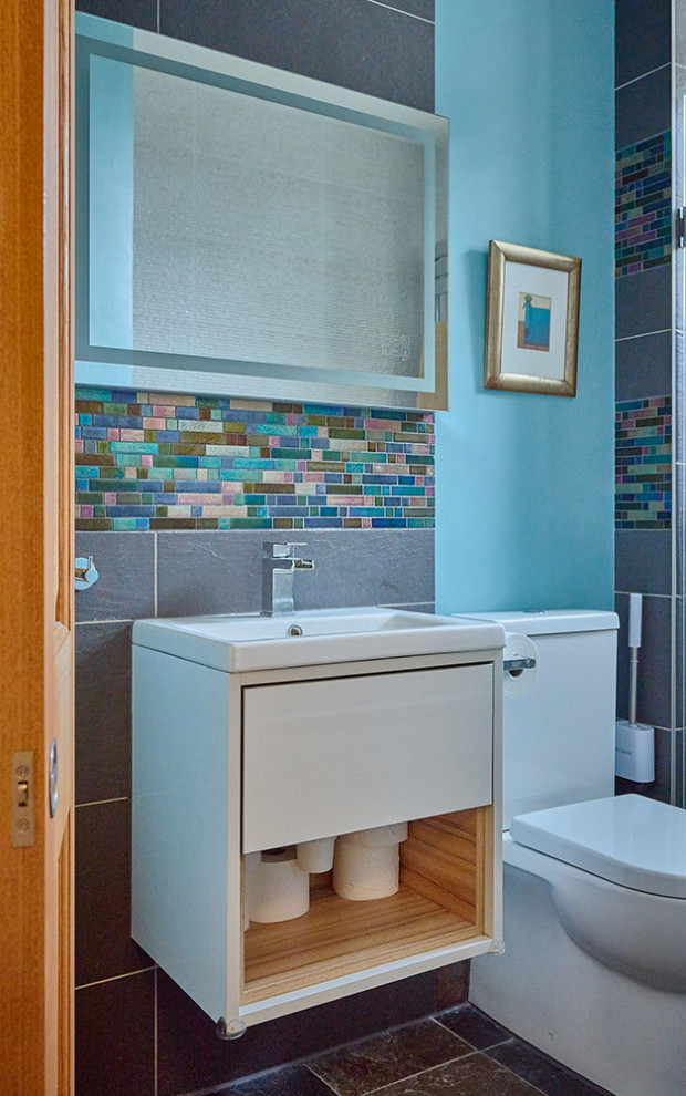 This is an example of a small contemporary grey and teal bathroom in London with a one-piece toilet, multi-coloured tiles, mosaic tiles, blue walls, terracotta flooring, a wall-mounted sink, multi-coloured floors, a wall niche and a single sink.
