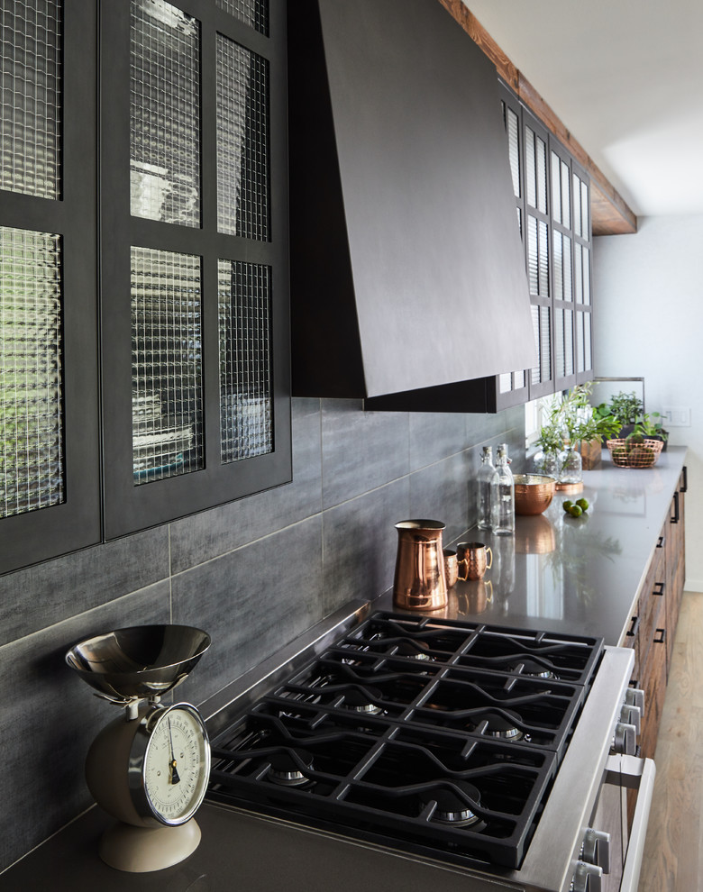 Large industrial galley eat-in kitchen in New York with an undermount sink, flat-panel cabinets, dark wood cabinets, grey splashback, black appliances, light hardwood floors, with island, beige floor and grey benchtop.