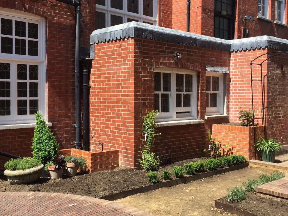 Design ideas for a mid-sized traditional courtyard full sun formal garden for summer in Sussex with a container garden and brick pavers.