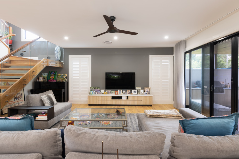 This is an example of a contemporary living room in Brisbane with grey walls, medium hardwood floors, a wall-mounted tv and brown floor.