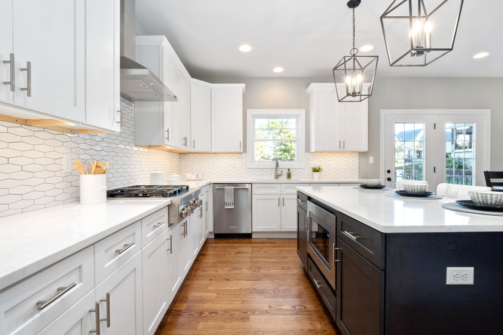 Transitional medium tone wood floor and brown floor kitchen photo in St Louis with shaker cabinets, white cabinets, quartz countertops, white backsplash, ceramic backsplash, stainless steel appliances, an island and white countertops