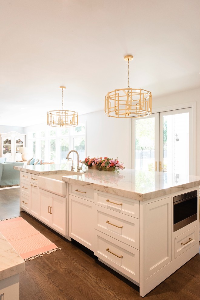 Large transitional l-shaped medium tone wood floor and brown floor open concept kitchen photo with a farmhouse sink, recessed-panel cabinets, white cabinets, quartzite countertops, white backsplash, stone slab backsplash, paneled appliances and an island