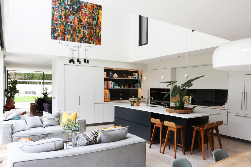 Photo of a contemporary l-shaped kitchen in Cambridgeshire with an undermount sink, flat-panel cabinets, white cabinets, black splashback, panelled appliances, light hardwood floors, with island, beige floor and white benchtop.