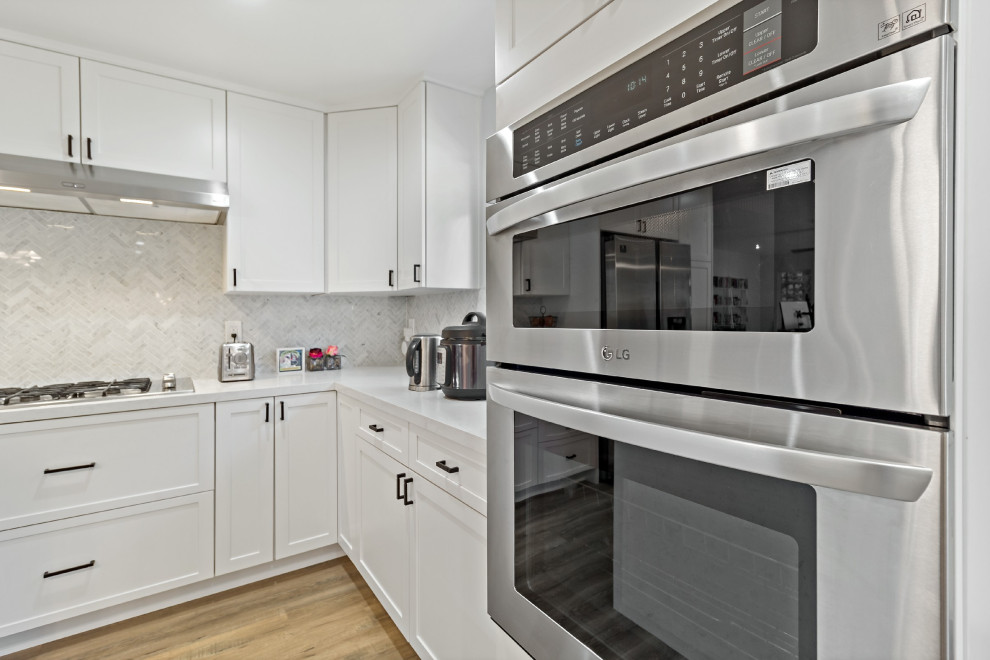 Bild på ett mycket stort skandinaviskt vit vitt kök, med en nedsänkt diskho, skåp i shakerstil, vita skåp, bänkskiva i kvartsit, vitt stänkskydd, stänkskydd i mosaik, svarta vitvaror, mörkt trägolv, en köksö och brunt golv