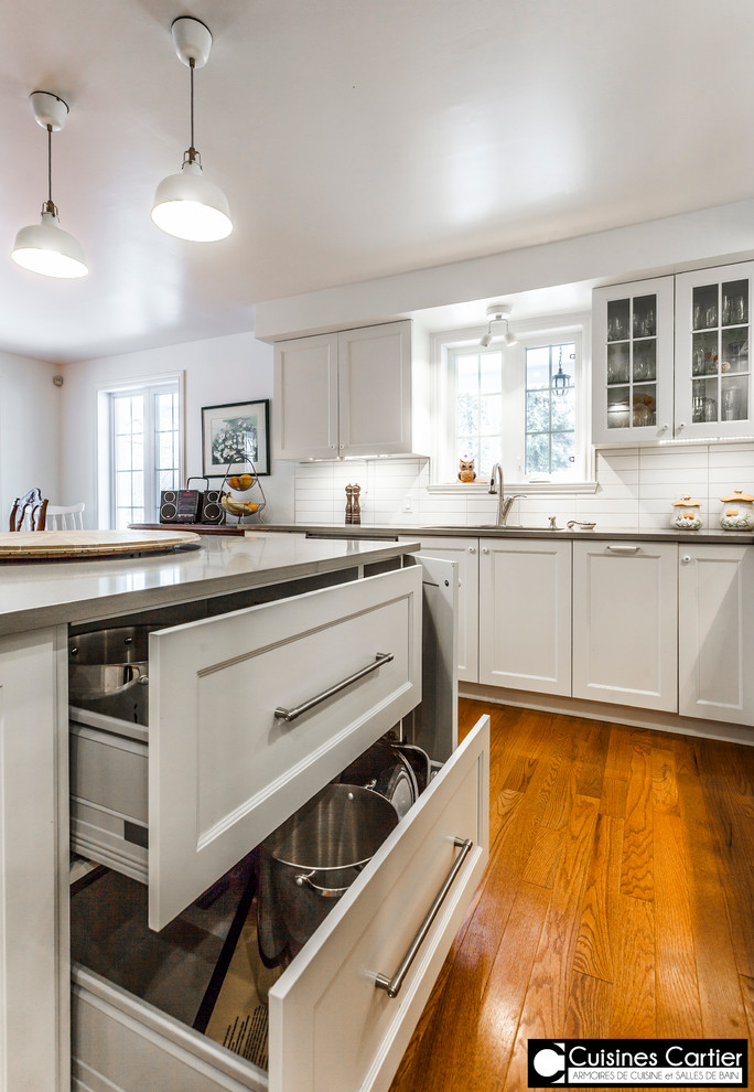 Example of a large transitional medium tone wood floor eat-in kitchen design in Montreal with a double-bowl sink, shaker cabinets, white cabinets, quartzite countertops, white backsplash, ceramic backsplash, stainless steel appliances and an island