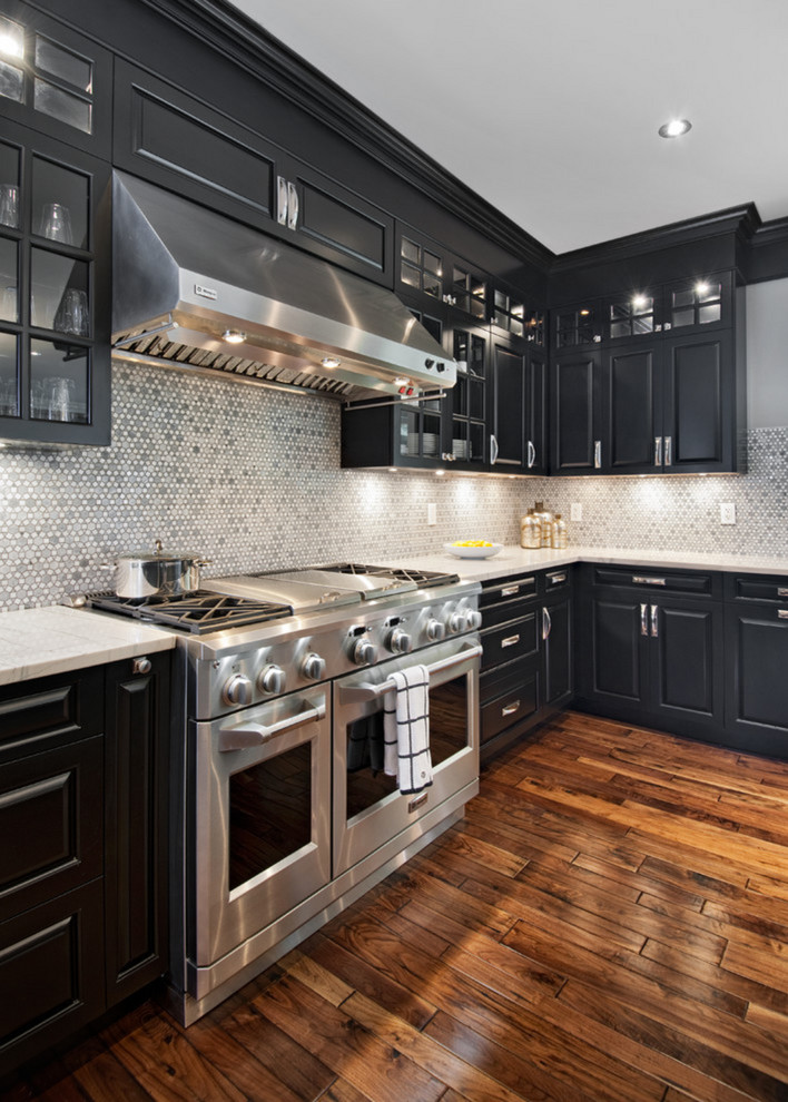 This is an example of a large country l-shaped eat-in kitchen in Orange County with a farmhouse sink, raised-panel cabinets, black cabinets, quartz benchtops, grey splashback, ceramic splashback, stainless steel appliances, dark hardwood floors and with island.