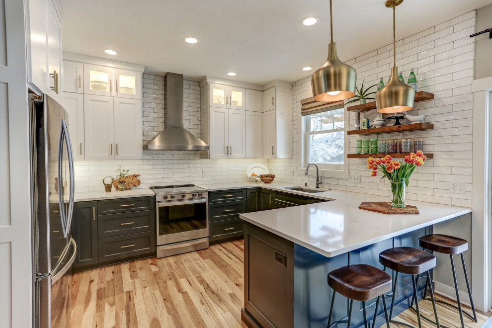 Photo of a mid-sized transitional u-shaped eat-in kitchen in Minneapolis with an undermount sink, recessed-panel cabinets, blue cabinets, quartz benchtops, white splashback, subway tile splashback, stainless steel appliances, light hardwood floors, a peninsula, brown floor and white benchtop.
