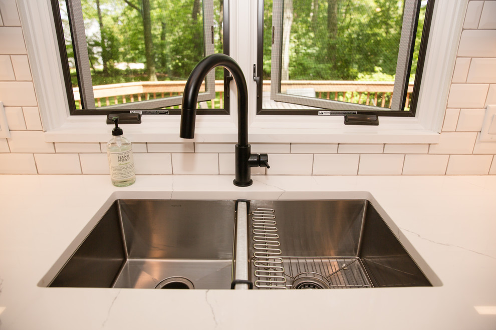Example of a mid-sized transitional galley medium tone wood floor and brown floor eat-in kitchen design with an undermount sink, shaker cabinets, white cabinets, solid surface countertops, white backsplash, ceramic backsplash, stainless steel appliances, a peninsula and white countertops