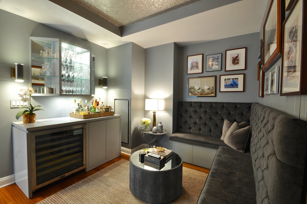 Design ideas for a mid-sized transitional single-wall seated home bar in New York with flat-panel cabinets, grey cabinets, solid surface benchtops, medium hardwood floors, no sink, brown floor and grey benchtop.