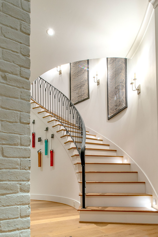 This is an example of a large transitional wood curved staircase in Houston with painted wood risers and metal railing.