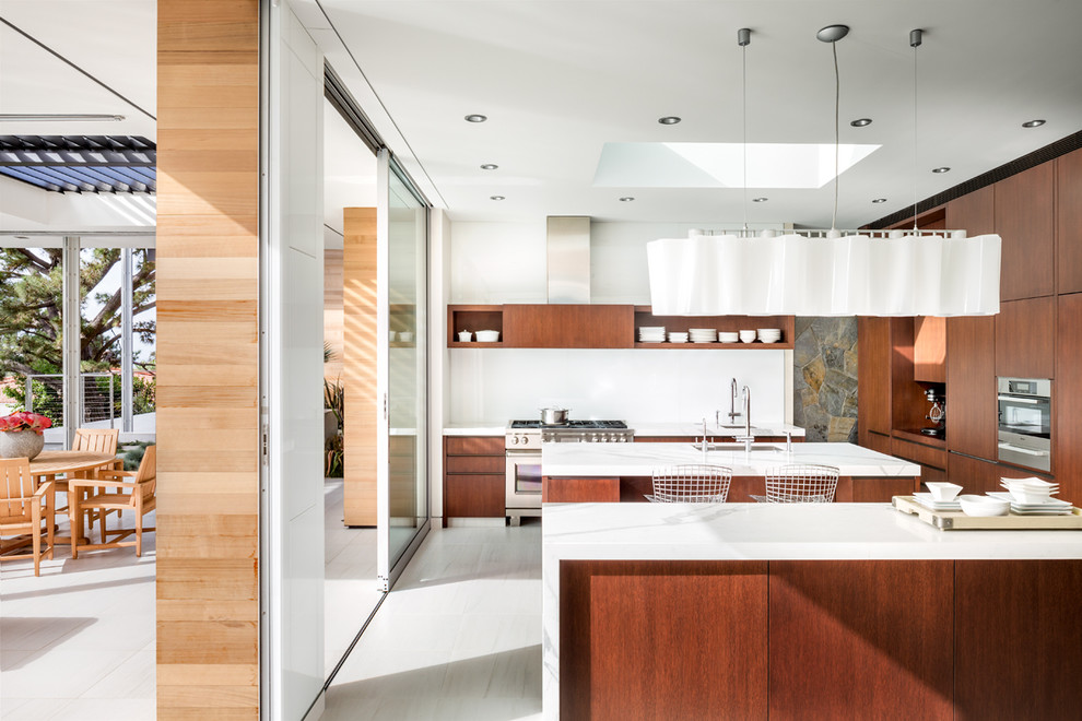 Design ideas for a large midcentury galley eat-in kitchen in Los Angeles with an undermount sink, flat-panel cabinets, medium wood cabinets, marble benchtops, white splashback, glass tile splashback, stainless steel appliances, ceramic floors, multiple islands and white floor.