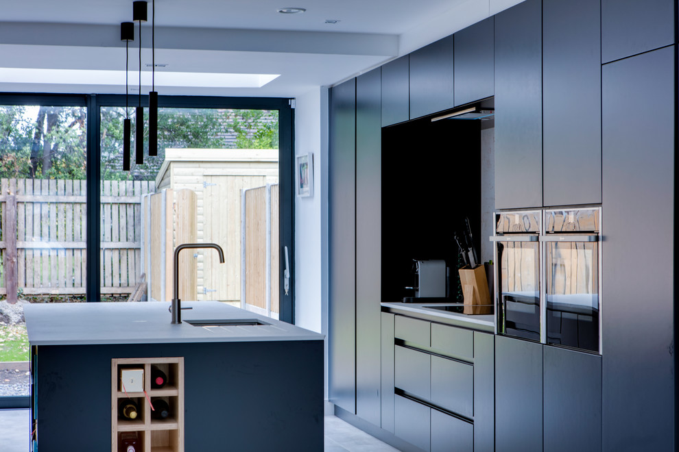 Photo of a mid-sized contemporary galley open plan kitchen in Dublin with a drop-in sink, flat-panel cabinets, blue cabinets, quartzite benchtops, grey splashback, stone slab splashback, stainless steel appliances, porcelain floors, with island, grey floor and grey benchtop.