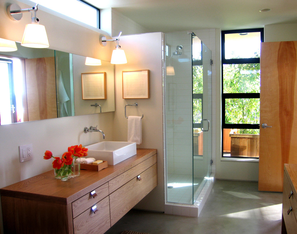 This is an example of a mid-sized modern master bathroom in Seattle with flat-panel cabinets, light wood cabinets, a corner shower, white tile, ceramic tile, white walls, concrete floors, a vessel sink, wood benchtops, grey floor and a hinged shower door.