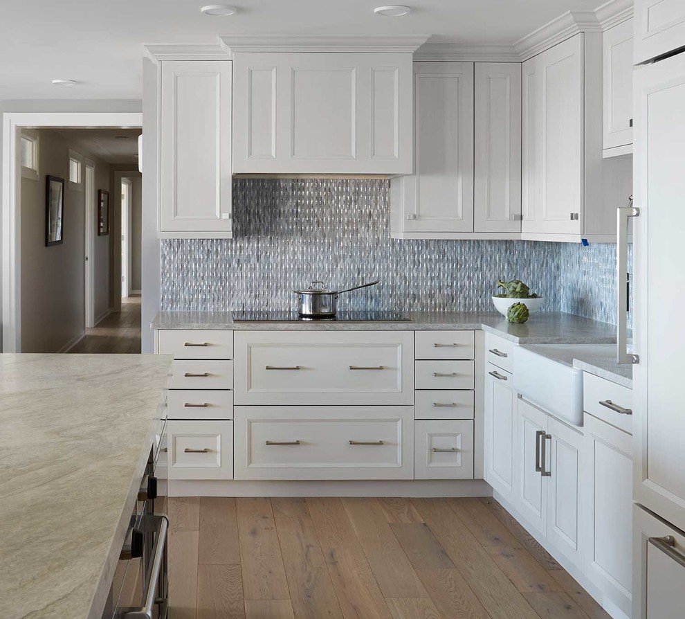 Large contemporary u-shaped open plan kitchen in Chicago with a farmhouse sink, recessed-panel cabinets, white cabinets, quartzite benchtops, blue splashback, glass tile splashback, stainless steel appliances, light hardwood floors, with island, brown floor and white benchtop.