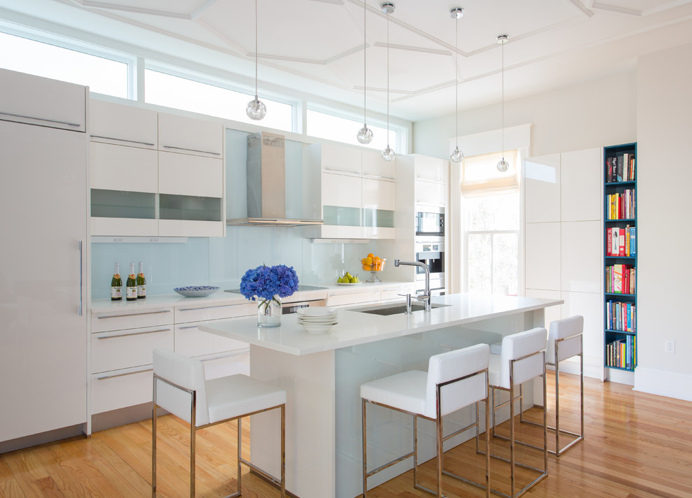 Photo of a mid-sized contemporary galley open plan kitchen in Boston with an undermount sink, flat-panel cabinets, white cabinets, blue splashback, glass sheet splashback, stainless steel appliances, medium hardwood floors, with island and solid surface benchtops.