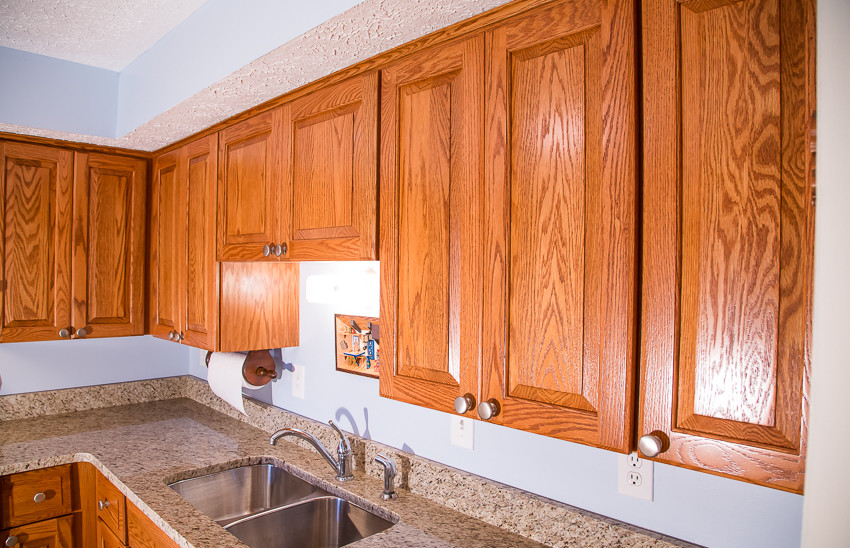 Small mountain style l-shaped kitchen photo in Baltimore with a double-bowl sink, raised-panel cabinets, medium tone wood cabinets, blue backsplash, white appliances and no island