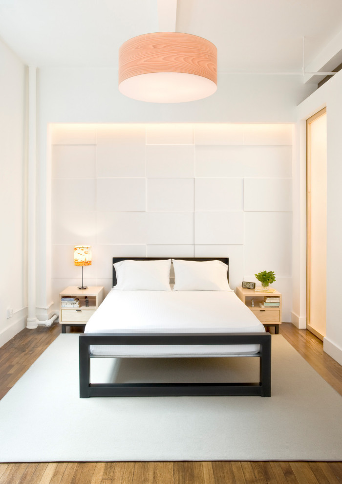 This is an example of a mid-sized contemporary loft-style bedroom in New York with white walls and medium hardwood floors.