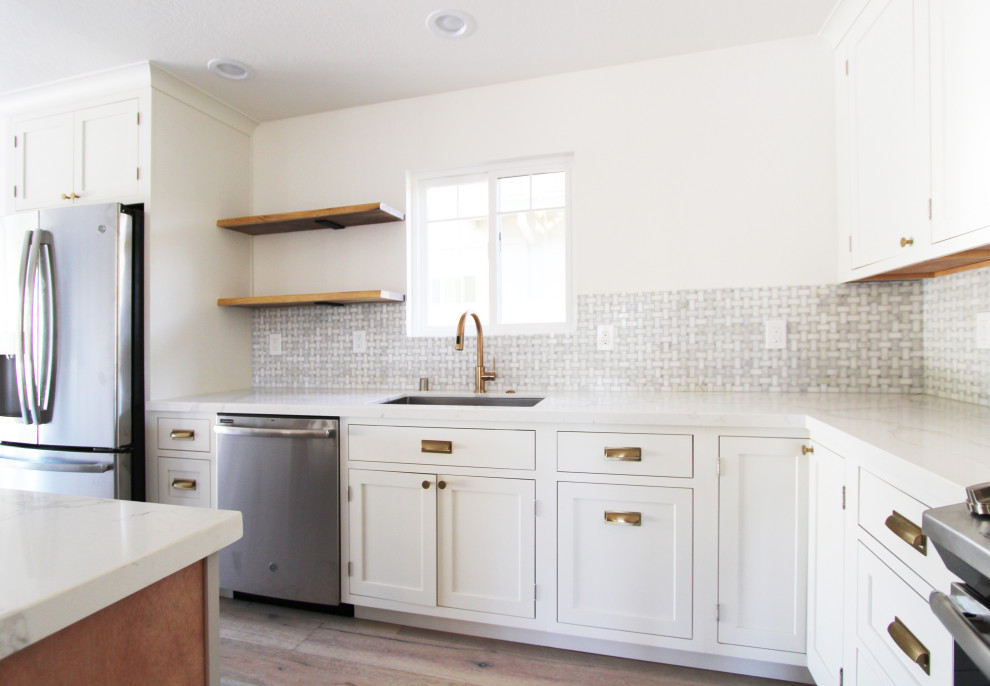 Open concept kitchen - mid-sized l-shaped light wood floor and brown floor open concept kitchen idea with an undermount sink, shaker cabinets, white cabinets, quartz countertops, gray backsplash, mosaic tile backsplash, stainless steel appliances, an island and white countertops