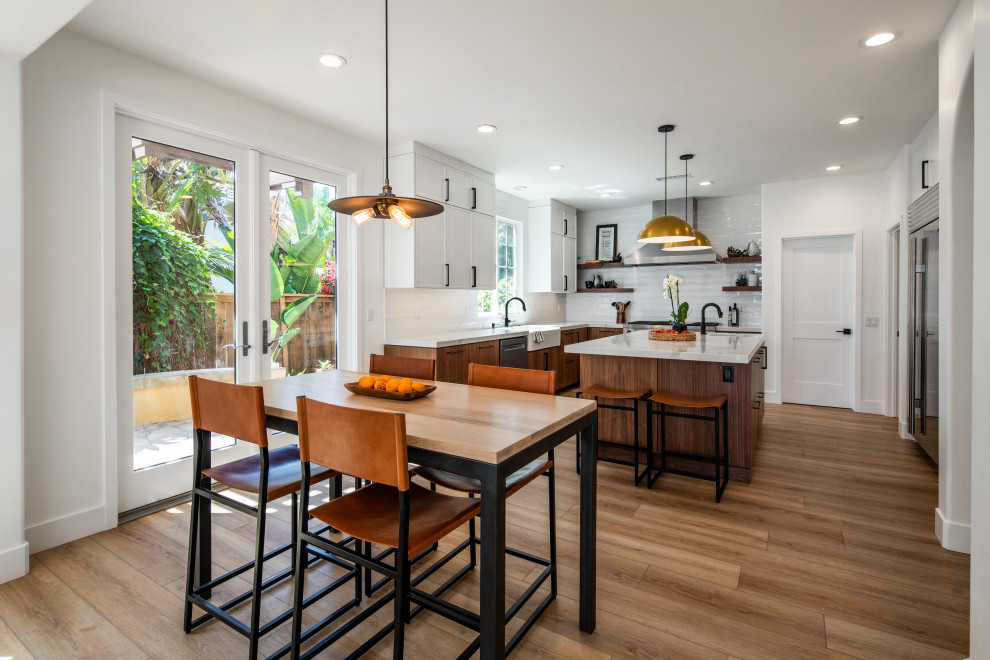 Mid-sized midcentury u-shaped open plan kitchen in San Diego with a farmhouse sink, flat-panel cabinets, medium wood cabinets, marble benchtops, white splashback, ceramic splashback, stainless steel appliances, laminate floors, with island, beige floor and white benchtop.
