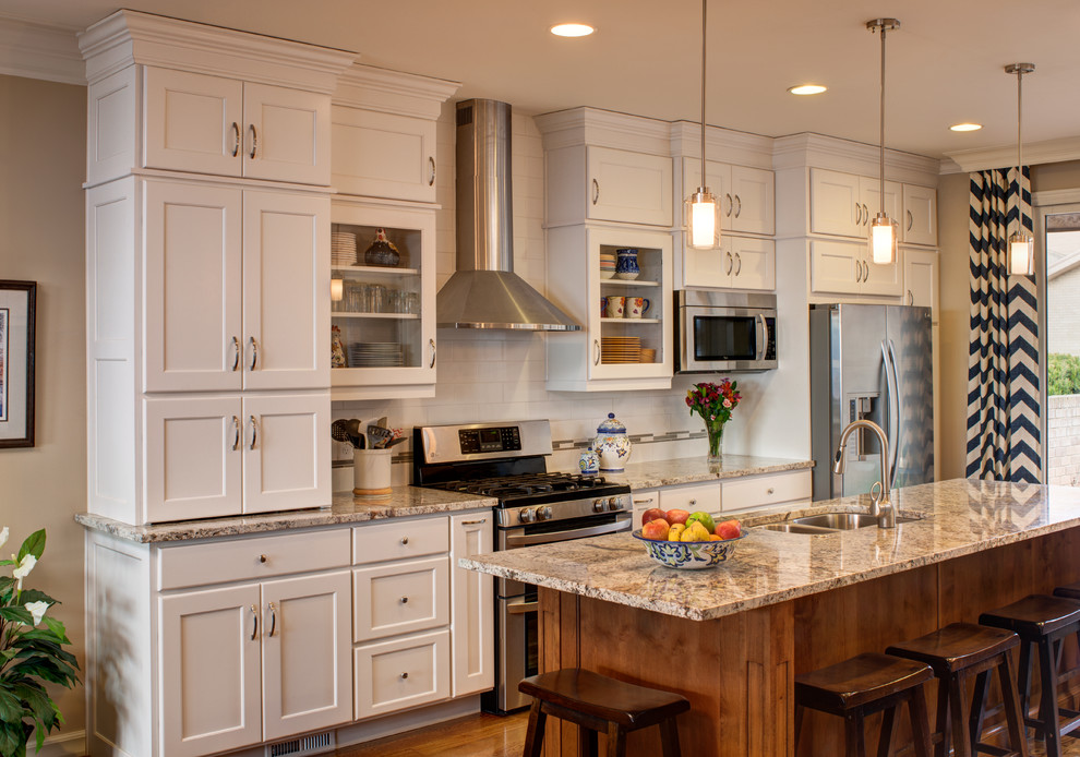 Example of a large transitional l-shaped light wood floor kitchen design in Denver with an undermount sink, shaker cabinets, light wood cabinets, granite countertops, beige backsplash, stone tile backsplash, stainless steel appliances and an island