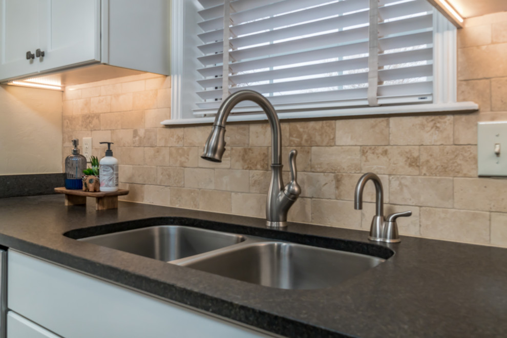Example of a transitional galley vinyl floor and beige floor eat-in kitchen design with a double-bowl sink, recessed-panel cabinets, white cabinets, granite countertops, beige backsplash, travertine backsplash, stainless steel appliances, a peninsula and black countertops