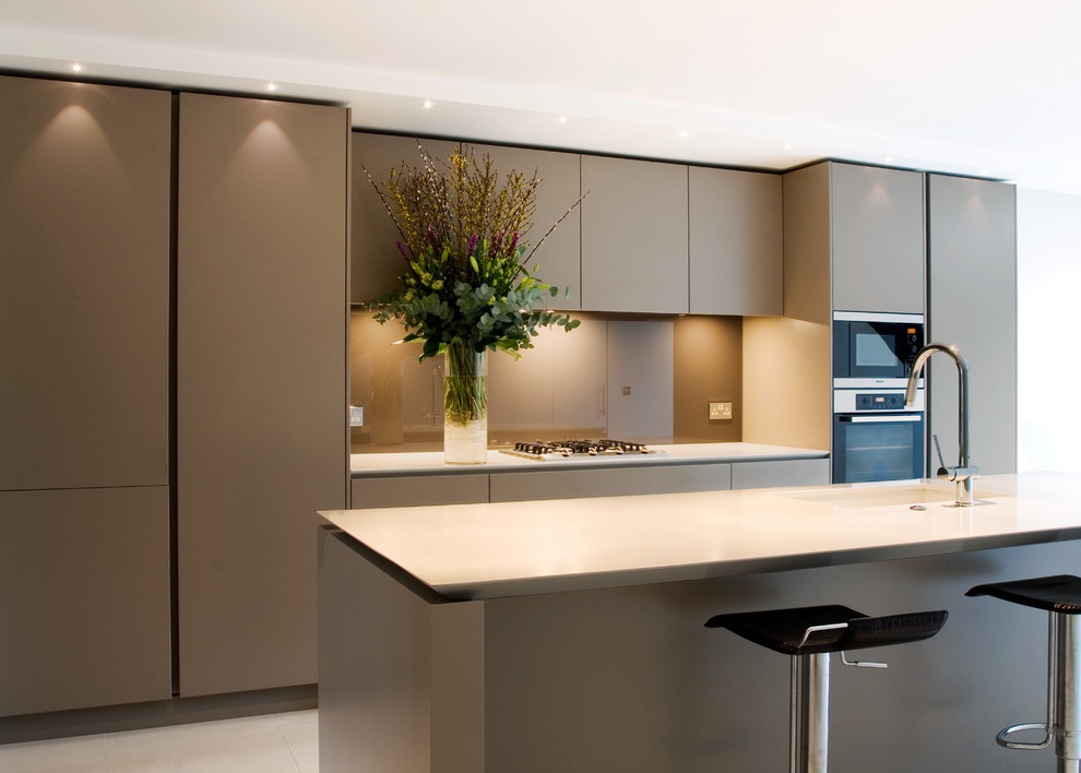 This is an example of a mid-sized contemporary eat-in kitchen in London with stainless steel appliances, with island, flat-panel cabinets, beige cabinets, quartz benchtops, beige splashback, glass sheet splashback, an undermount sink, ceramic floors and beige floor.