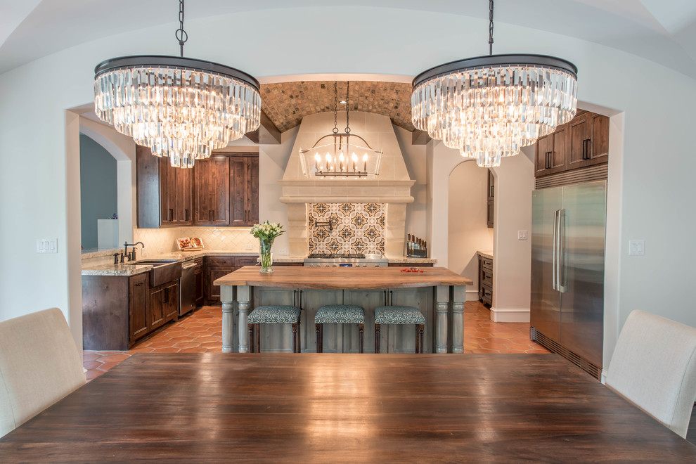 This is an example of a large mediterranean u-shaped open plan kitchen in Houston with a farmhouse sink, raised-panel cabinets, dark wood cabinets, granite benchtops, multi-coloured splashback, mosaic tile splashback, stainless steel appliances, terra-cotta floors, with island and orange floor.