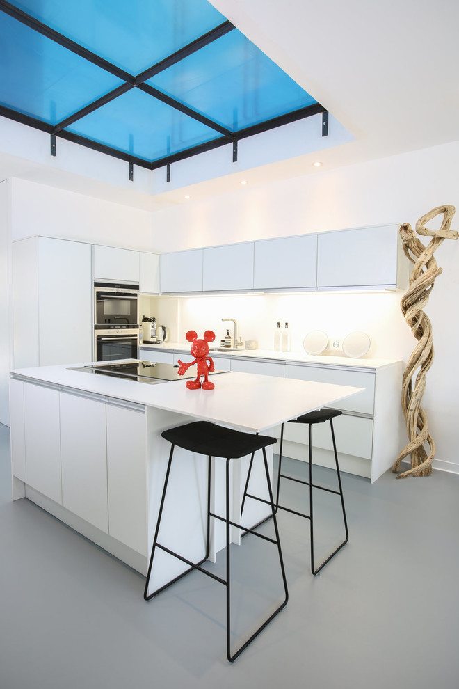 Inspiration for a mid-sized contemporary l-shaped kitchen in Paris with a single-bowl sink, white cabinets, concrete benchtops, white splashback, stone slab splashback, panelled appliances, concrete floors, with island, grey floor, white benchtop and flat-panel cabinets.