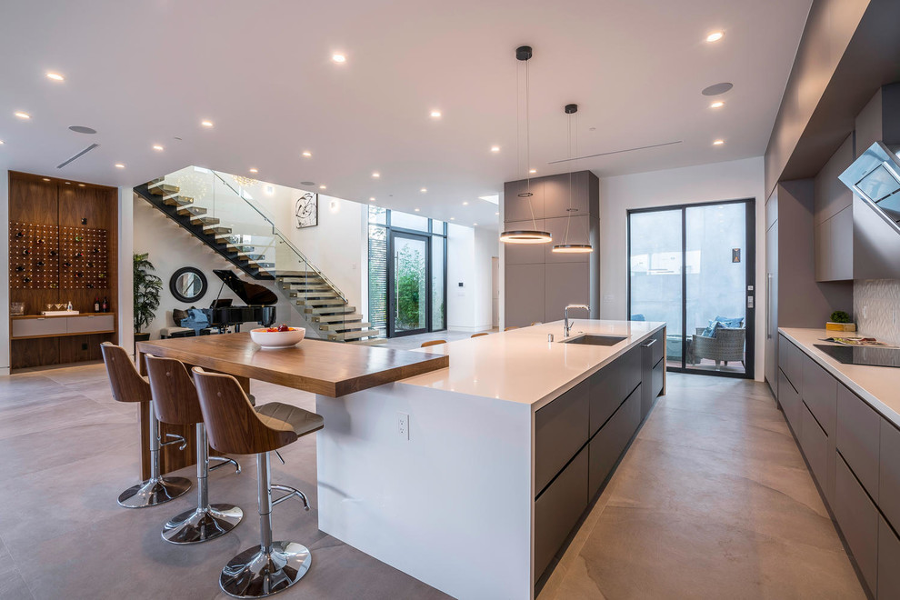 This is an example of an expansive contemporary l-shaped open plan kitchen in Los Angeles with an undermount sink, flat-panel cabinets, multiple islands, beige floor, solid surface benchtops, white splashback, grey cabinets, ceramic splashback, stainless steel appliances and concrete floors.