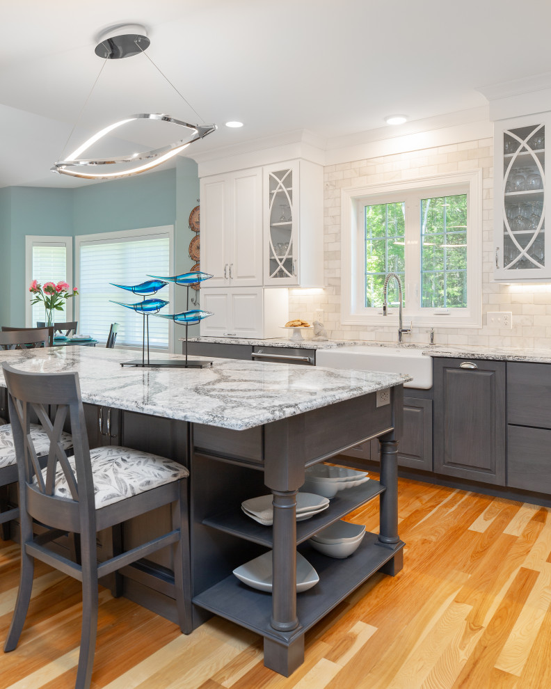 Example of a large transitional l-shaped light wood floor and brown floor eat-in kitchen design with a farmhouse sink, raised-panel cabinets, gray cabinets, granite countertops, white backsplash, marble backsplash, stainless steel appliances and an island