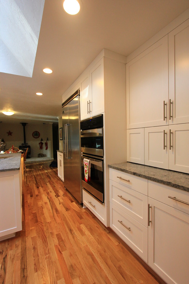 Example of a large transitional u-shaped light wood floor open concept kitchen design with an undermount sink, shaker cabinets, white cabinets, granite countertops, multicolored backsplash, mosaic tile backsplash, stainless steel appliances and an island