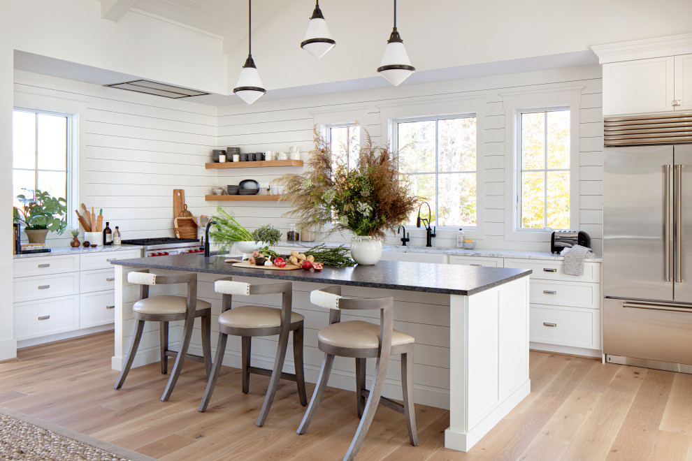 Lantlig inredning av ett stort grå grått l-kök, med släta luckor, en rustik diskho, vita skåp, marmorbänkskiva, vitt stänkskydd, stänkskydd i trä, rostfria vitvaror, ljust trägolv, en köksö och beiget golv