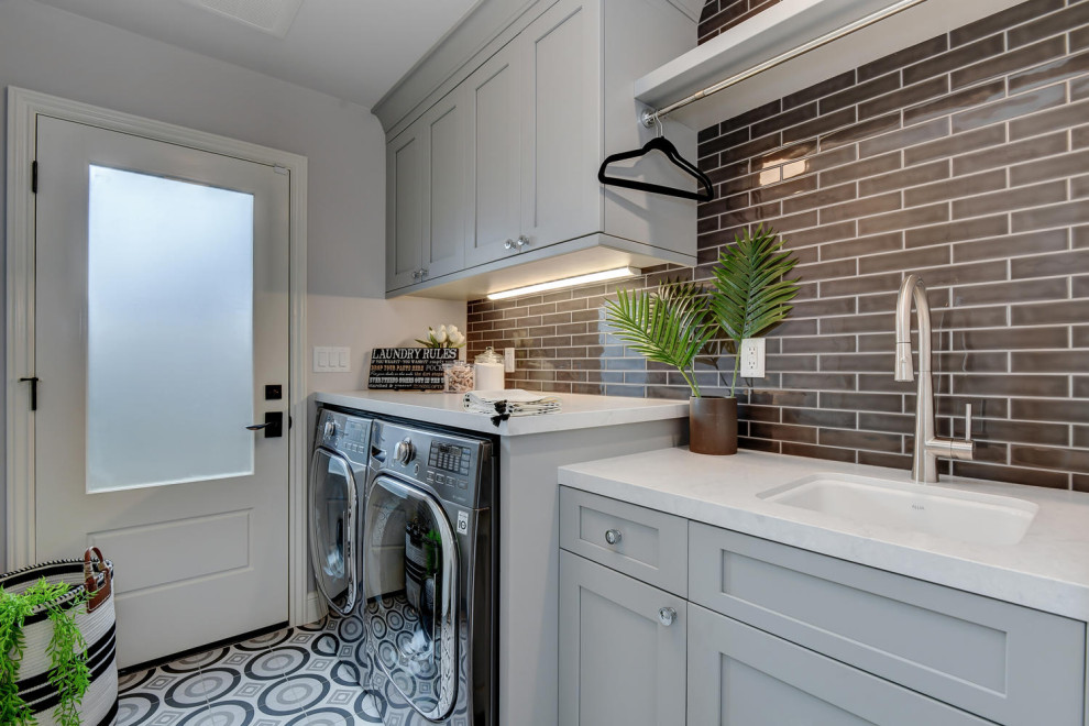 Inspiration for a mid-sized contemporary galley dedicated laundry room in San Francisco with an undermount sink, raised-panel cabinets, grey cabinets, quartz benchtops, grey walls, ceramic floors, a side-by-side washer and dryer, multi-coloured floor, grey benchtop, black splashback and glass sheet splashback.