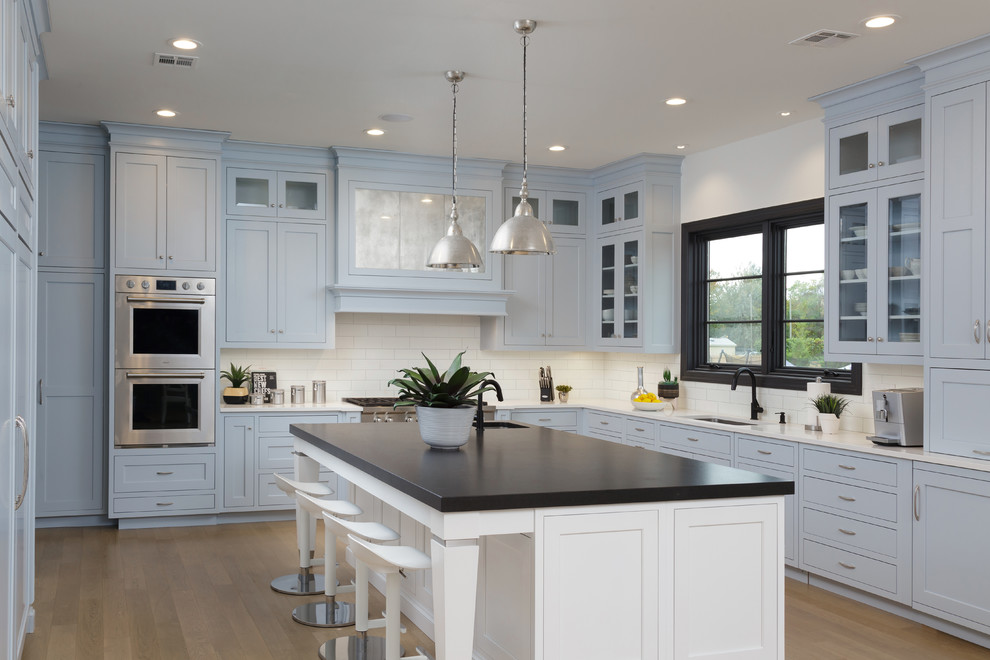 Transitional l-shaped light wood floor and beige floor kitchen photo with an undermount sink, shaker cabinets, white backsplash, subway tile backsplash, stainless steel appliances, an island, gray cabinets and white countertops