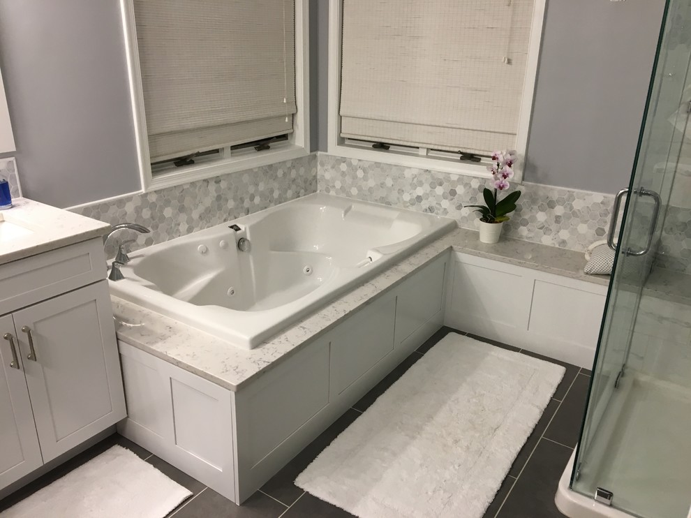 Photo of a large transitional master bathroom in Baltimore with white cabinets, shaker cabinets, a drop-in tub, a corner shower, gray tile, white tile, porcelain tile, purple walls, porcelain floors, an undermount sink, engineered quartz benchtops, grey floor, a hinged shower door and white benchtops.