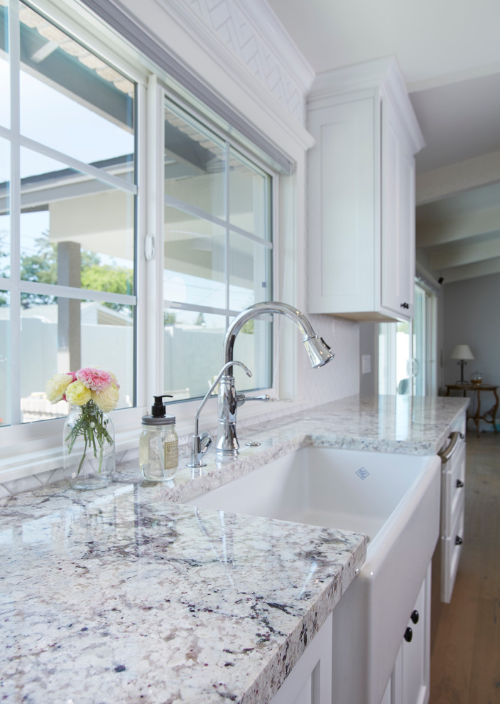 Inspiration for a mid-sized contemporary l-shaped kitchen in Phoenix with a farmhouse sink, shaker cabinets, white cabinets, granite benchtops, white splashback, subway tile splashback, stainless steel appliances, medium hardwood floors and with island.
