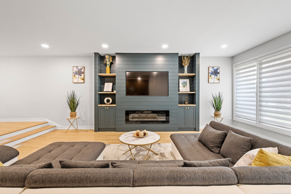 This is an example of a large contemporary open concept living room in Chicago with a library, blue walls, light hardwood floors, a standard fireplace and a built-in media wall.