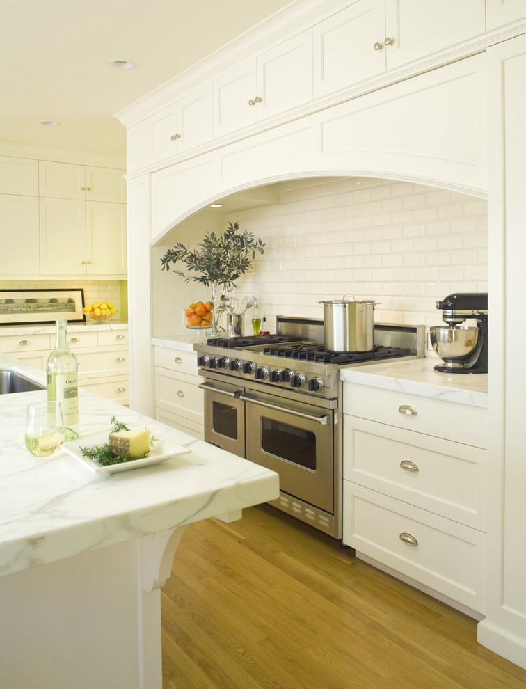 Design ideas for a mid-sized traditional l-shaped eat-in kitchen in San Francisco with stainless steel appliances, subway tile splashback, an undermount sink, recessed-panel cabinets, white cabinets, marble benchtops, white splashback, medium hardwood floors and with island.