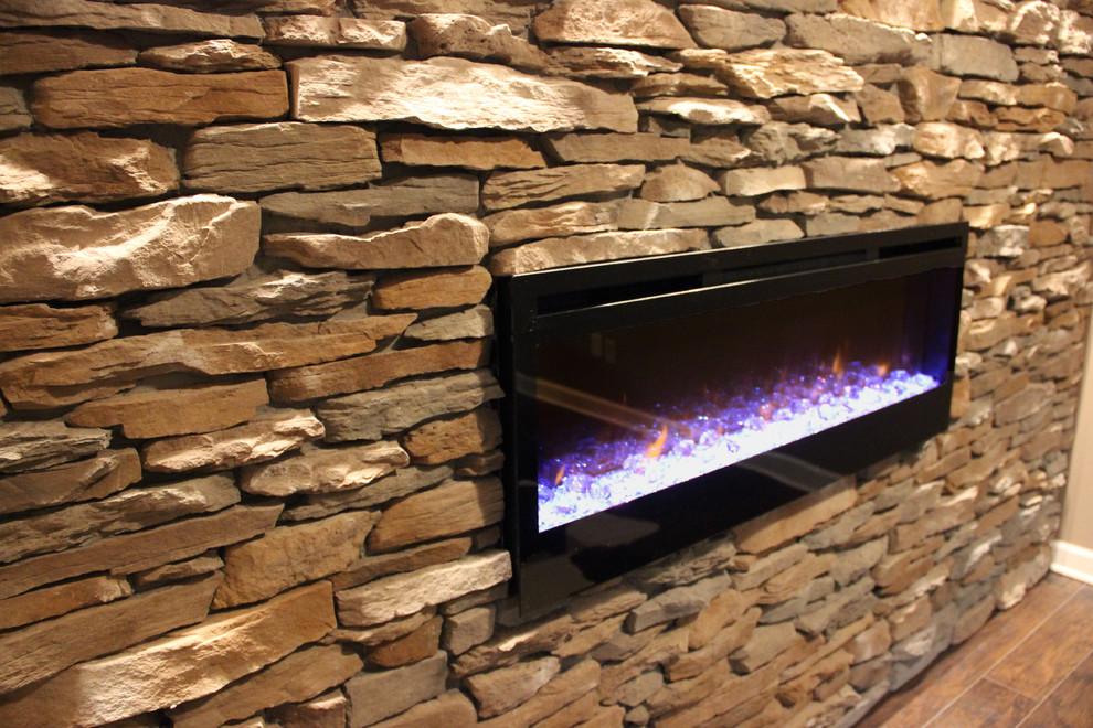 Example of a large mountain style underground laminate floor and brown floor basement design with beige walls, a stone fireplace and a ribbon fireplace