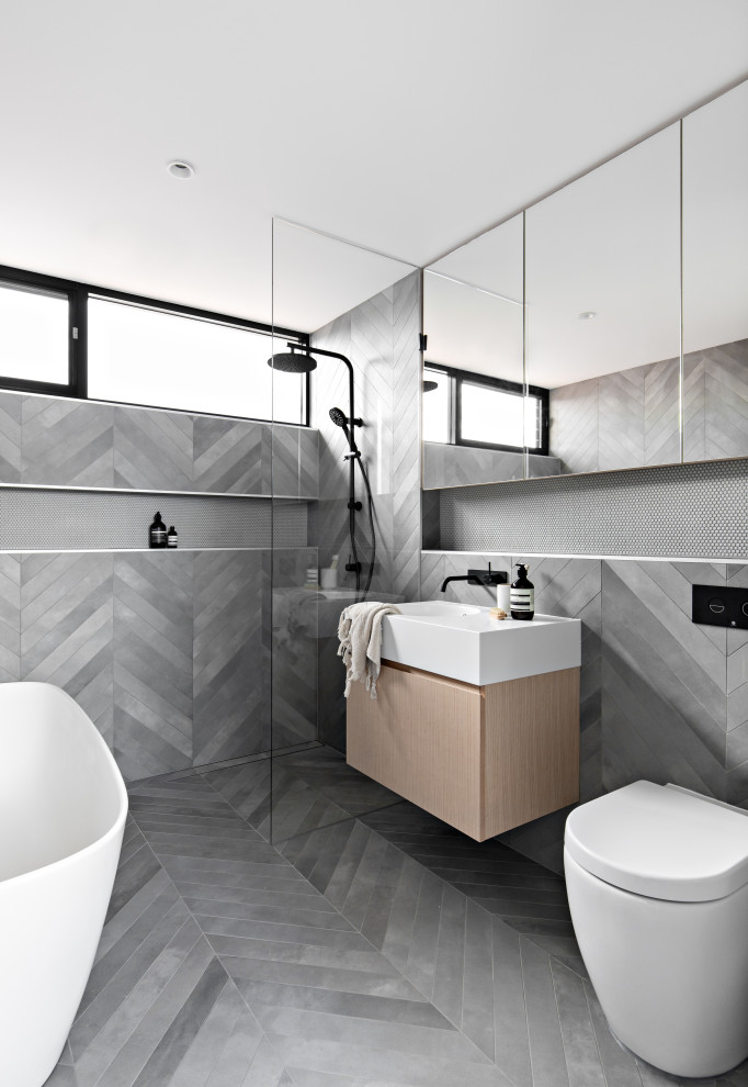 Photo of a contemporary master bathroom in Sydney with flat-panel cabinets, light wood cabinets, a freestanding tub, a curbless shower, a one-piece toilet, gray tile, grey walls, an integrated sink, grey floor, an open shower, white benchtops, a single vanity and a floating vanity.