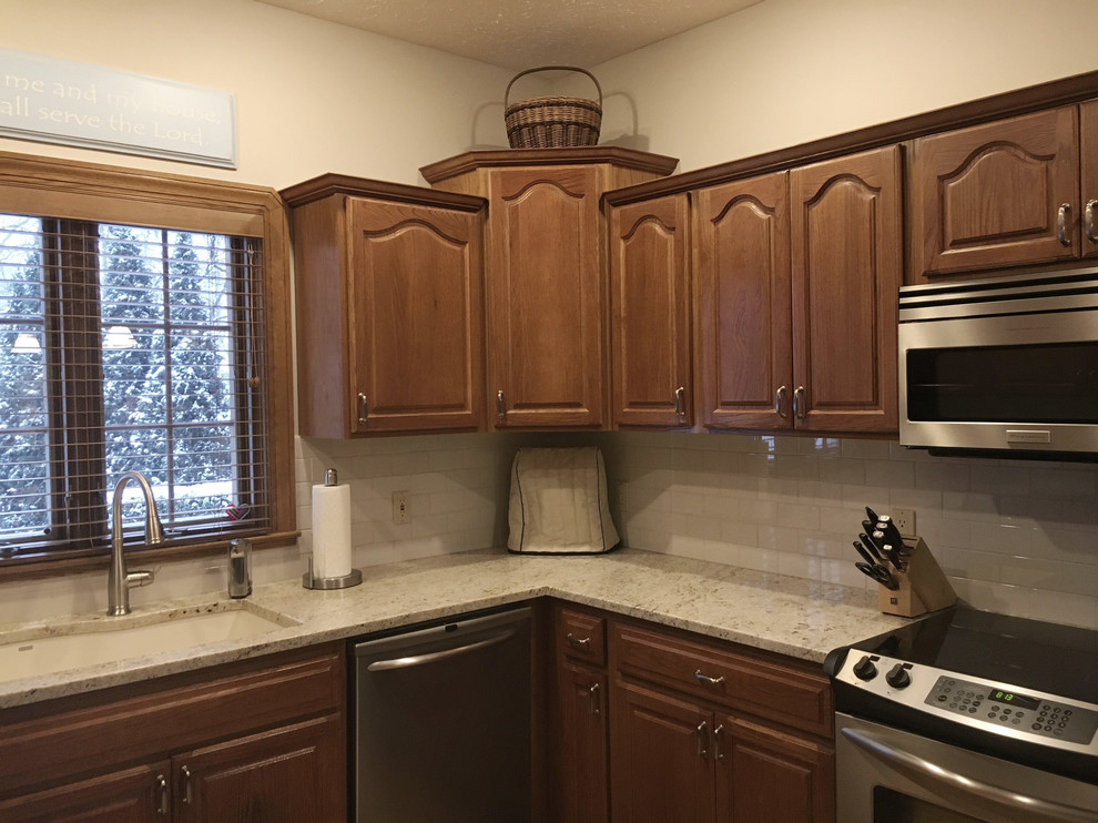 Example of a large transitional u-shaped medium tone wood floor eat-in kitchen design with an undermount sink, raised-panel cabinets, medium tone wood cabinets, granite countertops, white backsplash, ceramic backsplash, stainless steel appliances and an island