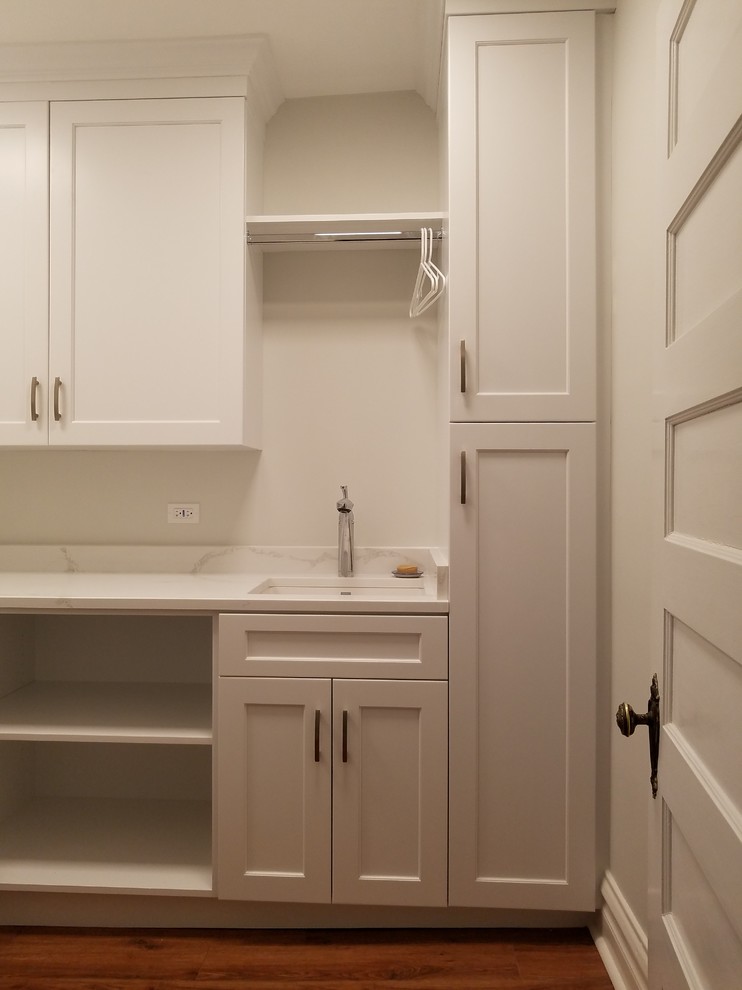 Design ideas for a mid-sized transitional l-shaped dedicated laundry room in Chicago with an undermount sink, recessed-panel cabinets, white cabinets, quartz benchtops, white walls, medium hardwood floors, a side-by-side washer and dryer, brown floor and white benchtop.