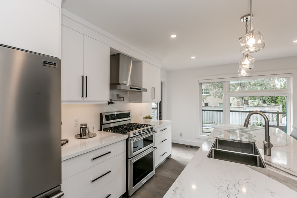 This is an example of a mid-sized modern single-wall open plan kitchen in Other with a double-bowl sink, shaker cabinets, white cabinets, white splashback, stainless steel appliances, medium hardwood floors, with island, brown floor and white benchtop.