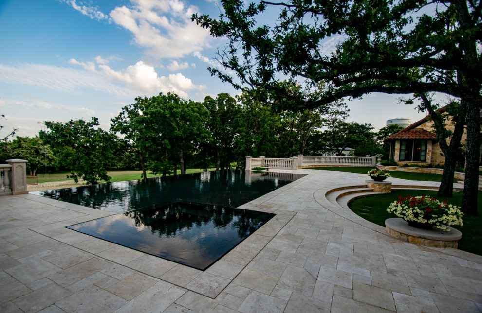 Cette photo montre une grande piscine à débordement et arrière nature sur mesure avec des pavés en pierre naturelle.