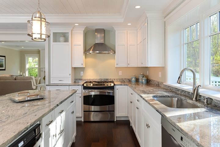 This is an example of a large beach style l-shaped eat-in kitchen in Boston with an undermount sink, beaded inset cabinets, white cabinets, quartz benchtops, beige splashback, stainless steel appliances, dark hardwood floors, with island and brown floor.